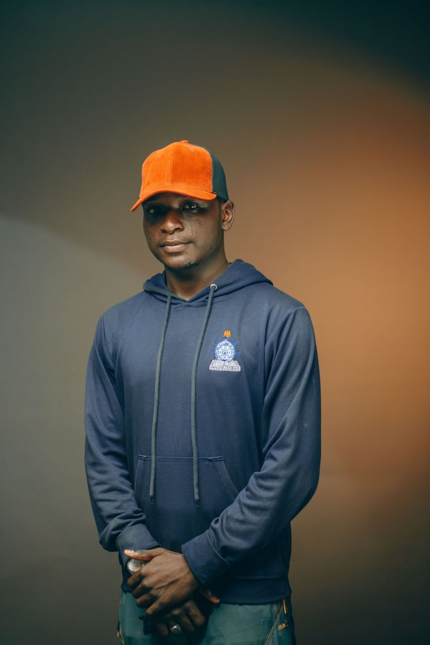 Portrait of a young man wearing a hoodie and cap in a studio setting with a warm background.